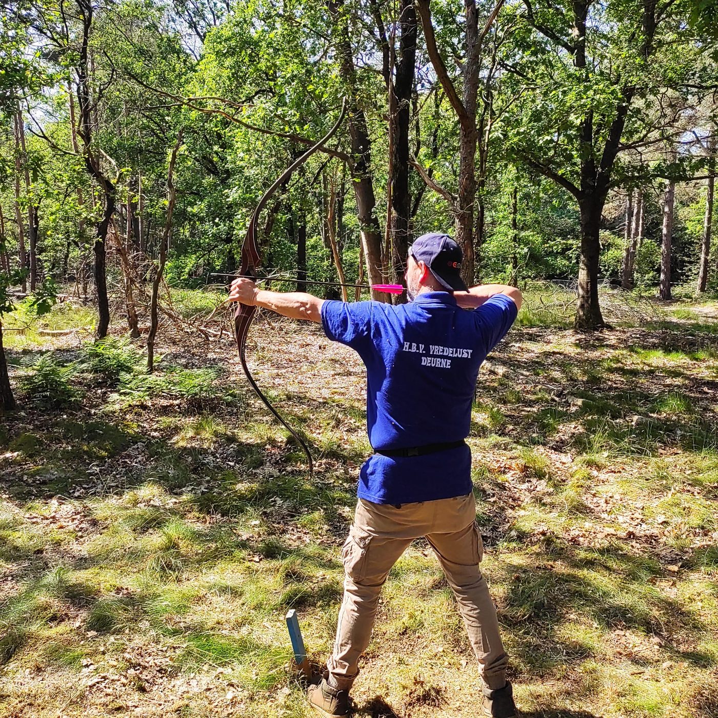 Een schutter in clubshirt schiet buiten tussen de bomen