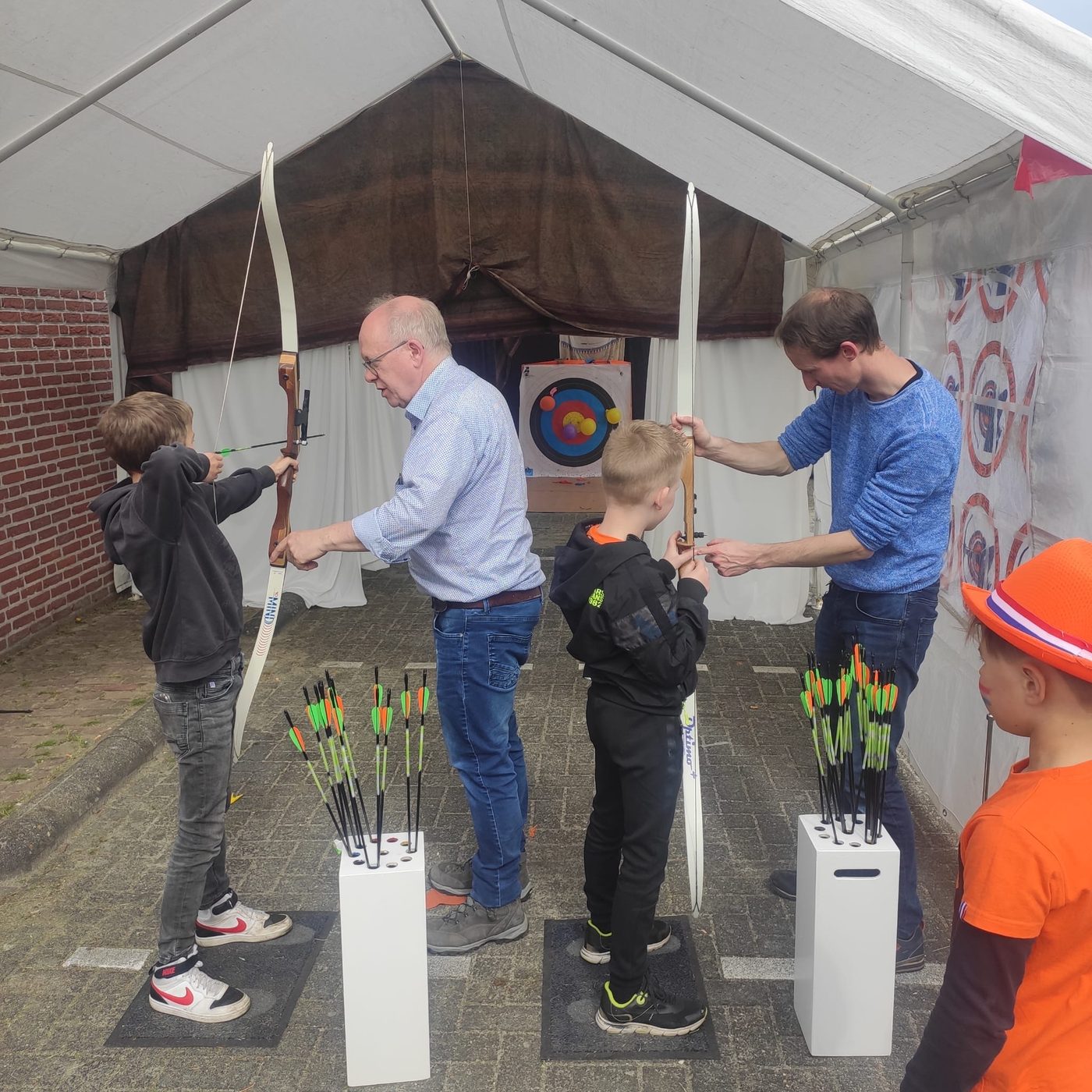 Kinderen proberen boogschieten onder begeleiding tijdens de Koningsmarkt